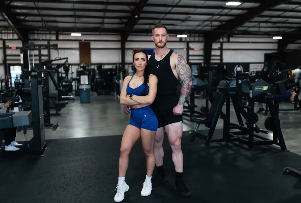 Fit woman and muscular man standing confidently with arms crossed inside a gym, promoting fitness and wellness at Evolve HRT & Wellness in The Woodlands, TX